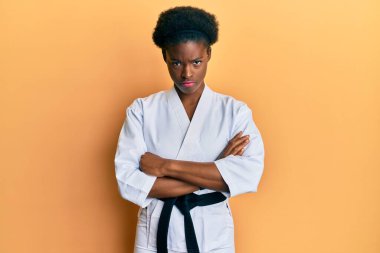 Genç Afrikalı Amerikalı kız karate kimonosu giyiyor ve siyah kuşak kuşkucu ve gergin, yüzünde çapraz kollu tasvip etmeyen bir ifade var. negatif kişi. 