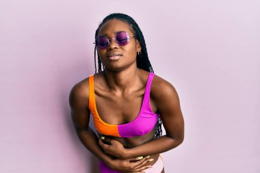 Genç Afro-Amerikan kadın bikini ve güneş gözlüğü takıyor. Midesi bulanıyor, acı verici bir hastalık yüzünden. Ağrı kavramı. 