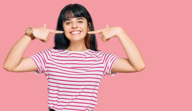 Günlük kıyafetler giyen, neşeli gülümseyen, parmaklarıyla ve ağzıyla işaret eden genç İspanyol kız. diş sağlığı kavramı. 