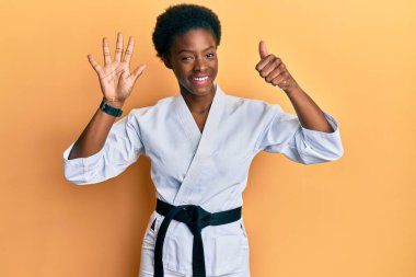 Karate kimonosu ve siyah kuşak giyen Afrikalı genç bir kız altı numaralı parmaklarını gösterip gülümserken kendinden emin ve mutlu görünüyor.. 