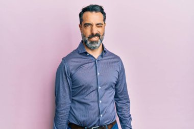 Orta yaşlı, sakallı, iş kıyafetleri giyen, kameraya seksi bir ifadeyle bakan, neşeli ve mutlu yüzlü bir adam.. 