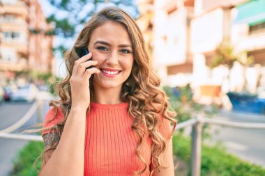 Genç sarışın kız gülümsüyor. Şehirde akıllı telefondan konuşuyor..
