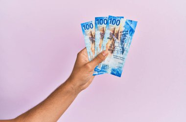 İspanyol el, izole edilmiş pembe arka planda 100 İsviçre frangı banknot tutuyor..