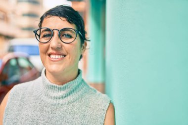 Genç ve cüsseli bir kadın gülümsüyor. Şehrin duvarına yaslanmaktan mutlu..