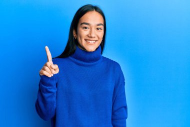 Sıradan bir kazak giyen Asyalı genç bir kadın başarılı bir fikri işaret ediyor. Heyecanlı ve mutlu. Bir numara.. 