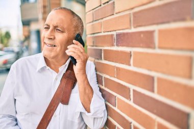 Kıdemli gri saçlı işadamı gülümsüyor. Şehirdeki akıllı telefondan mutlu bir şekilde konuşuyor..