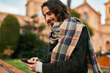 Genç İspanyol adam şehirde akıllı telefon kullanarak mutlu gülümsüyor..