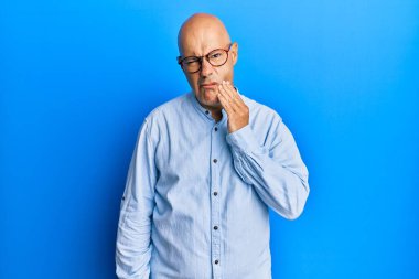 Orta yaşlı, kel bir adam diş ağrısı ya da diş ağrısı yüzünden ağzıyla dokunan sıradan kıyafetler ve gözlük takıyor. dişçi 