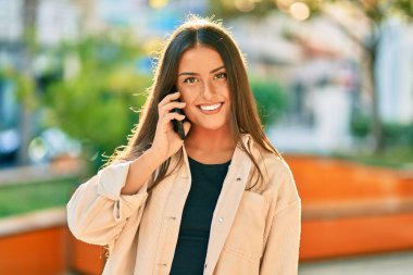 Genç İspanyol kız gülümsüyor. Parktaki akıllı telefondan konuşarak mutlu oluyor..