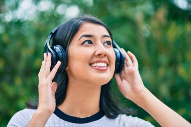 Genç İspanyol kadın gülümseyerek şehirde kulaklık takarak müzik dinliyor..