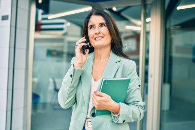 Kendine güvenen, şık takım elbiseli bir iş kadını sokakta dikilip telefonda konuşuyor.