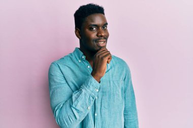 Yakışıklı, sıradan kıyafetler giyen, kameraya kendinden emin, kolları çapraz ve çenesi kalkık bir şekilde bakan siyahi bir adam. Olumlu düşünmek. 