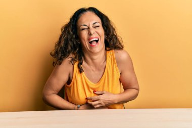 Güzel, orta yaşlı bir kadın, gündelik giysiler içinde masada oturuyor, gülümsüyor ve kahkahalarla gülüyor.. 