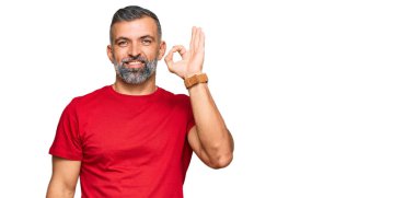 Orta yaşlı, sıradan kıyafetler giyen, gülümseyen, el ve parmaklarıyla imza atan yakışıklı bir adam. başarılı ifade. 