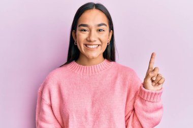 Genç Asyalı kadın, günlük kışlık süveter giyip bir fikir veya soruyla gülümsüyor ve mutlu bir yüzle işaret ediyor. 