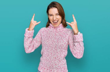 Kışlık yün kazak giyen genç beyaz kız çılgın bir ifadeyle bağırıyor elleri havada rock sembolü yapıyor. Müzik yıldızı. ağır müzik konsepti. 