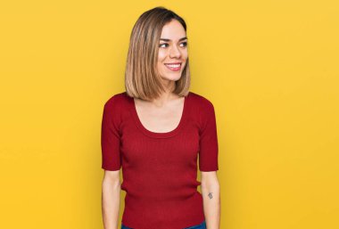 Sıradan kıyafetler giyen genç sarışın kız yüzünde gülümsemeyle yan yana bakıyor, doğal bir ifade. Kendinden emin gülen. 