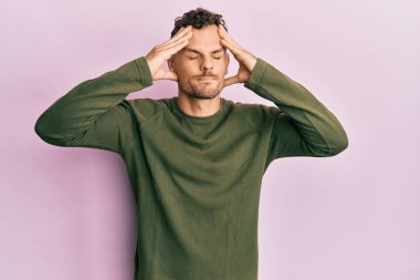 Latin asıllı genç bir adam elleri kafasında günlük kıyafetler giyiyor, stres yüzünden baş ağrısı çekiyor. migren ağrısı. 