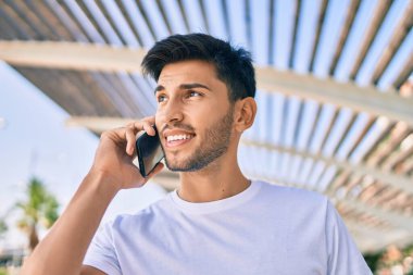 Genç Latin adam gülümsüyor ve şehirde akıllı telefondan konuşuyor..