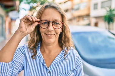 Orta yaşlı, beyaz bir kadın şehirde mutlu bir şekilde dikiliyor..