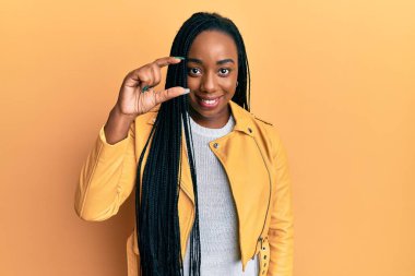 Rahat bir ceket giyen, gülümseyen, kendine güvenen, el hareketi yapan, parmaklarıyla işaret yapan ve kameraya bakan Afro-Amerikan genç bir kadın. ölçüm kavramı. 
