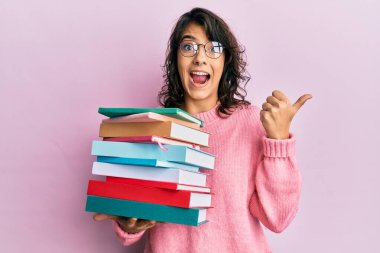 Genç İspanyol kadın elinde bir yığın kitapla baş parmağını kaldırıyor ve ağzı açık gülümsüyor. 