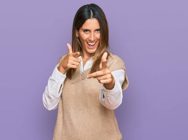 Günlük kıyafetler giymiş genç bir kadın mutlu ve komik yüzüyle kamerayı işaret ediyor. iyi enerji ve titreşimler. 