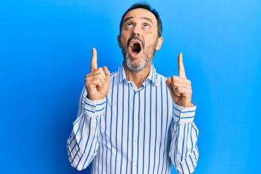 Orta yaşlı, sıradan kıyafetler giyen, şaşkın şaşkın bakan, parmaklarıyla işaret eden ve kollarını kaldıran bir İspanyol.. 