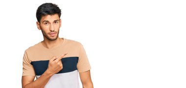 Gündelik giysiler giymiş genç yakışıklı bir adam el parmağı ile yan tarafı işaret ederek ciddi ve sakin bir yüz ifadesi sergiliyor. 