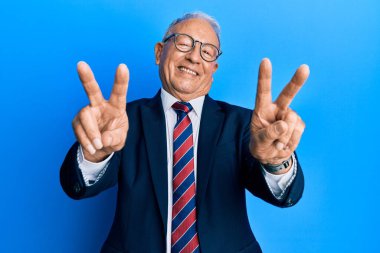 Takım elbiseli, kravatlı, ağzı açık gülümseyen ve parmaklarını zafer işareti yapan son sınıf beyaz adam. İki numara.. 