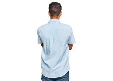 Genç, yakışıklı, Afro-Amerikalı, sıradan kıyafetler giymiş, arkasını dönüp kollarını kavuşturmuş. 