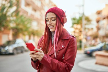 Beyaz kız şehirde akıllı telefon ve kulaklık kullanarak mutlu bir şekilde gülümsüyor..