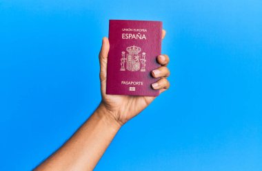 İspanyol pasaportlu bir adamın elleri mavi arka planda..