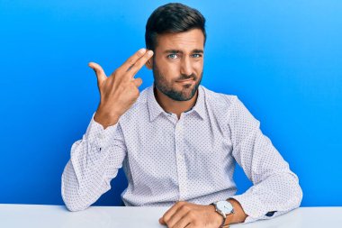 İş kıyafetleri giymiş yakışıklı İspanyol bir adam masaya oturmuş kendini vuruyor ve kendini öldürüyor. Silah gibi el ve parmakları işaret ediyor. İntihar jesti.. 