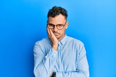 Gündelik kıyafetler ve gözlük takan genç İspanyol adam çapraz kollu depresyondan sıkılmış ve yorgun göründüğünü düşünüyor.. 