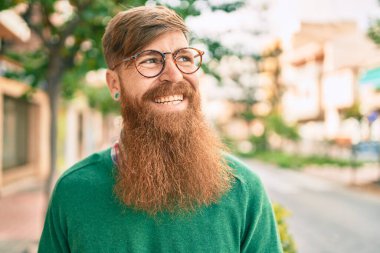 Kızıl sakallı genç İrlandalı adam şehirde mutlu bir şekilde yürürken gülümsüyor..