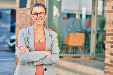 Sarışın iş kadını kollarını kavuşturup şehirde mutlu mesut gülümsüyor..