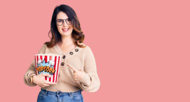 Güzel, genç, esmer bir kadın patlamış mısır yiyor. Gülümsüyor, mutlu bir şekilde işaret ediyor. 