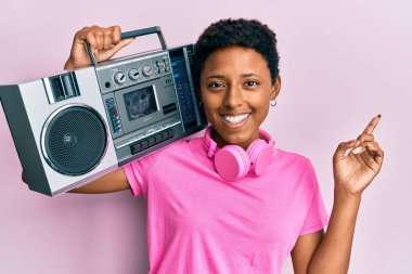 Genç Afrikalı Amerikalı kız, müzik kutusunu tutuyor, gülümsüyor, mutlu bir şekilde elini ve parmağını yana doğru uzatıyordu. 