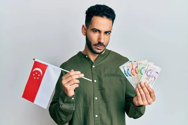 Young hispanic man holding singapore flag and dollars depressed and worry for distress, crying angry and afraid. sad expression.