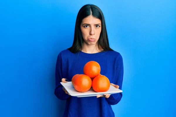 Mujer Hispana Joven Sosteniendo Plato Con Naranjas Frescas Deprimidas Preocupadas —  Fotos de Stock