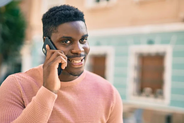 Genç Afrikalı Amerikalı gülümseyen mutlu bir adam şehirdeki akıllı telefondan konuşuyor..