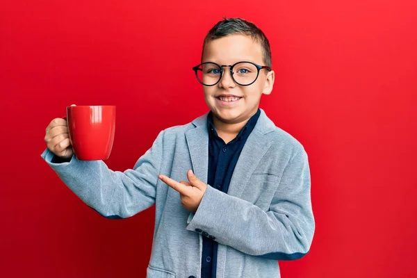 Mały Chłopiec Okularach Pijący Czerwonego Kubka Uśmiechający Się Szczęśliwy Wskazując — Zdjęcie stockowe