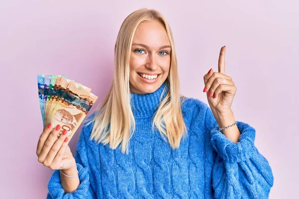 Mladá Blondýnka Drží Kanadské Dolary Ukazující Prstem Nahoru Úspěšným Nápadem — Stock fotografie