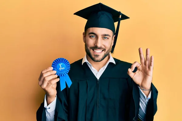 Jovem Hispânico Vestindo Roupão Formatura Segurando Emblema Lugar Fazendo Sinal — Fotografia de Stock