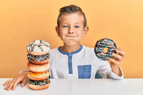Adorable caucasian kid eating doughnuts for breakfast puffing cheeks with funny face. mouth inflated with air, catching air.
