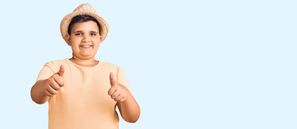夏の帽子をかぶっている小さな男の子とハワイの水着は 手で積極的なジェスチャーをすることを承認し 親指を上げて笑顔と成功のために幸せ 勝者のジェスチャー — ストック写真