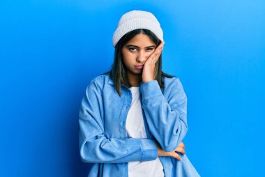 Tatlı yün şapka takan genç Latin kadın kollarını kavuşturup depresyondan sıkılmış ve yorgun görünüyor.. 