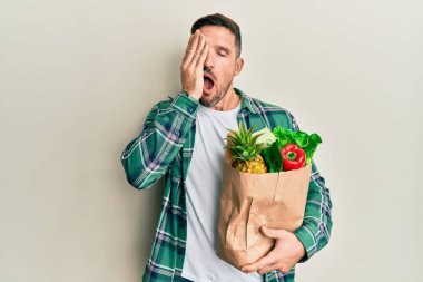 Sakallı yakışıklı bir adam, elinde poşetle market alışverişi yapıyor. Yüzünün yarısını, gözünü ve ağzını eliyle kapatmaktan yorulmuş. Yüzüm acıyor.. 