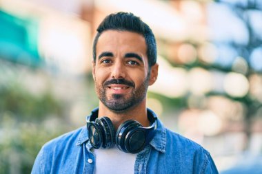 Şehirde kulaklık takarak mutlu gülümseyen genç İspanyol adam..